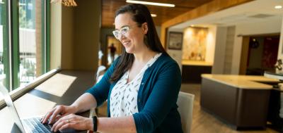 Woman sits in cafe window working on laptop